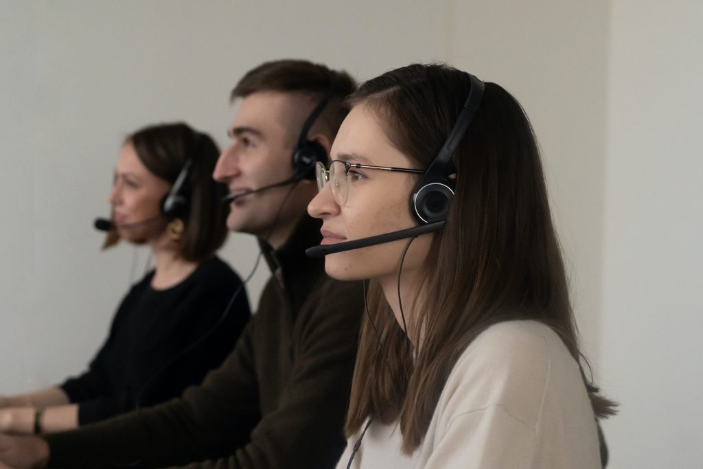 Vue latérale de jeunes opérateurs positifs en tenue décontractée avec des écouteurs et un microphone sur un lieu de travail lumineux.