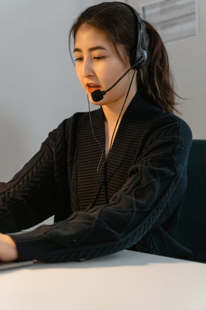 Femme asiatique professionnelle dans un rôle d'assistance à la clientèle, portant un casque d'écoute et se concentrant sur son travail.