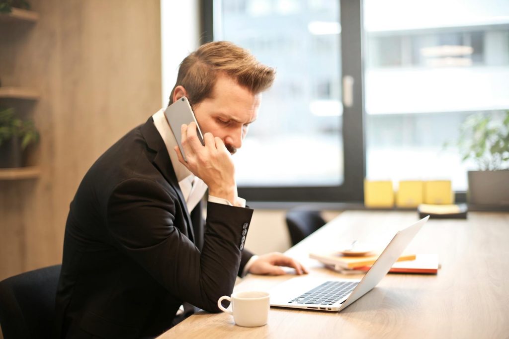 Un homme d'affaires en costume passe un appel téléphonique tout en travaillant sur un ordinateur portable dans un bureau moderne.